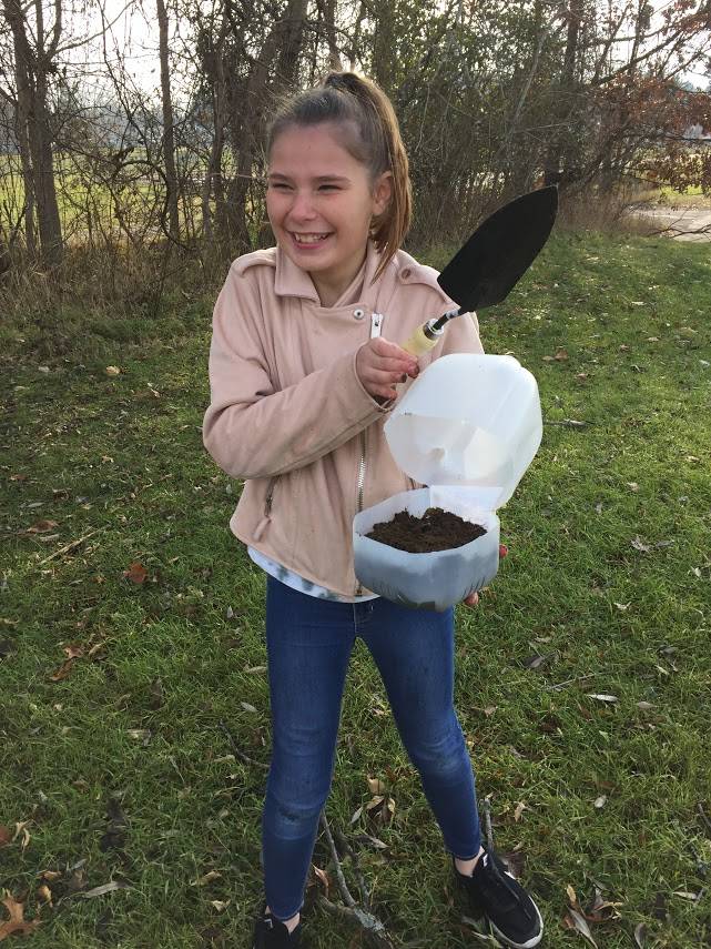 Student holds shovel and container of soil